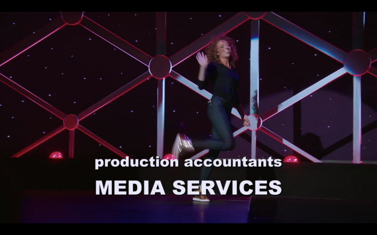 Michelle Wolf kicks a heel up and waves at the end of her 2017 special "Nice Lady" on HBO.   Text on screen reads "production accountants media services" but that's not why I posted the picture.